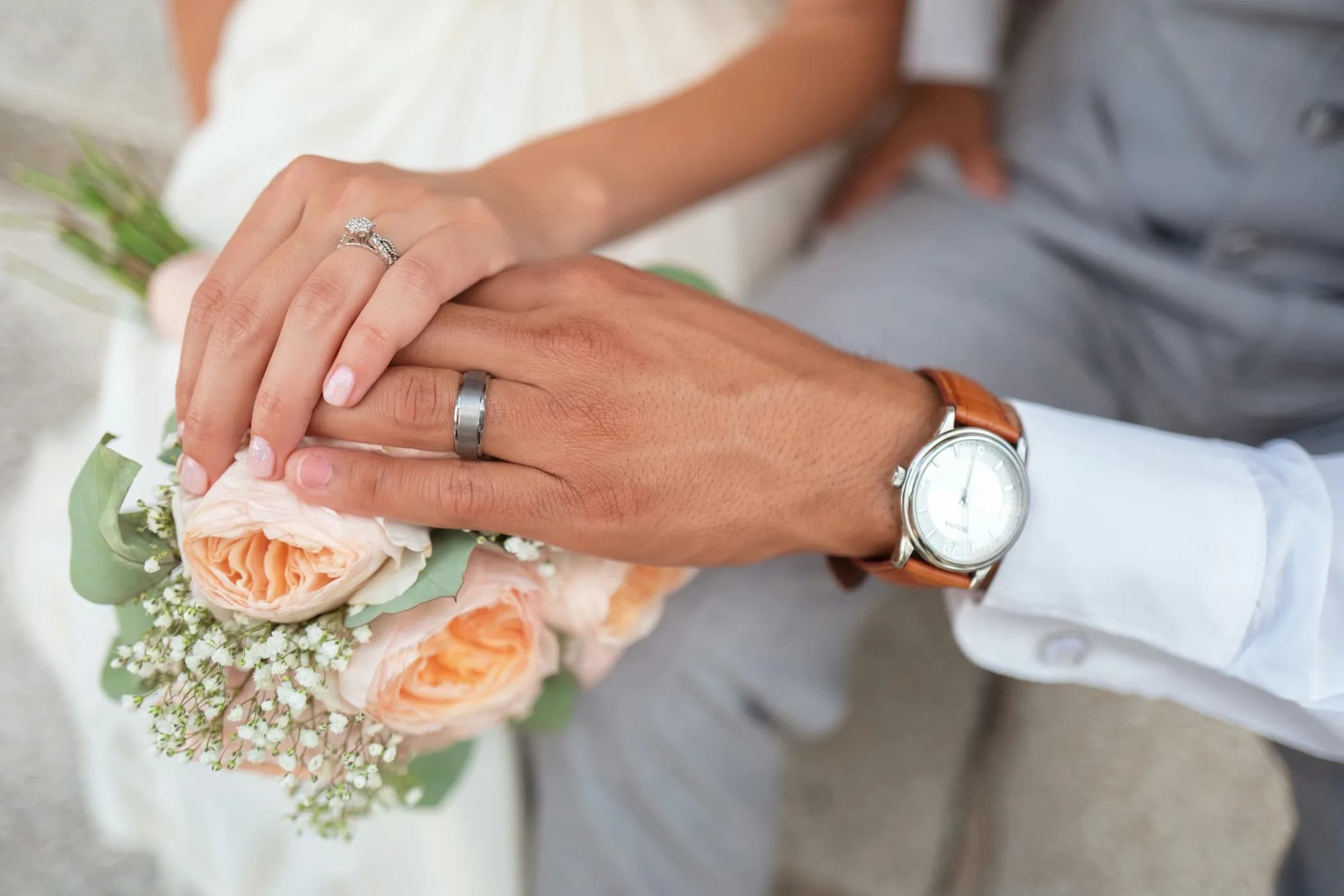 Newlyweds' hands touching over a bouquet of roses at a civil wedding ceremony, wedding rings visible — the moment when ceremony music matters most